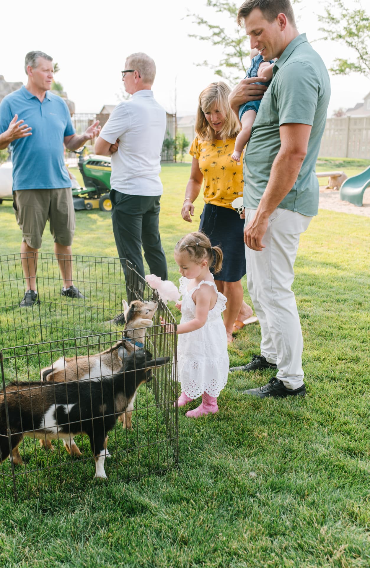 Family and kids gathered around the petting zoo pen in a backyard